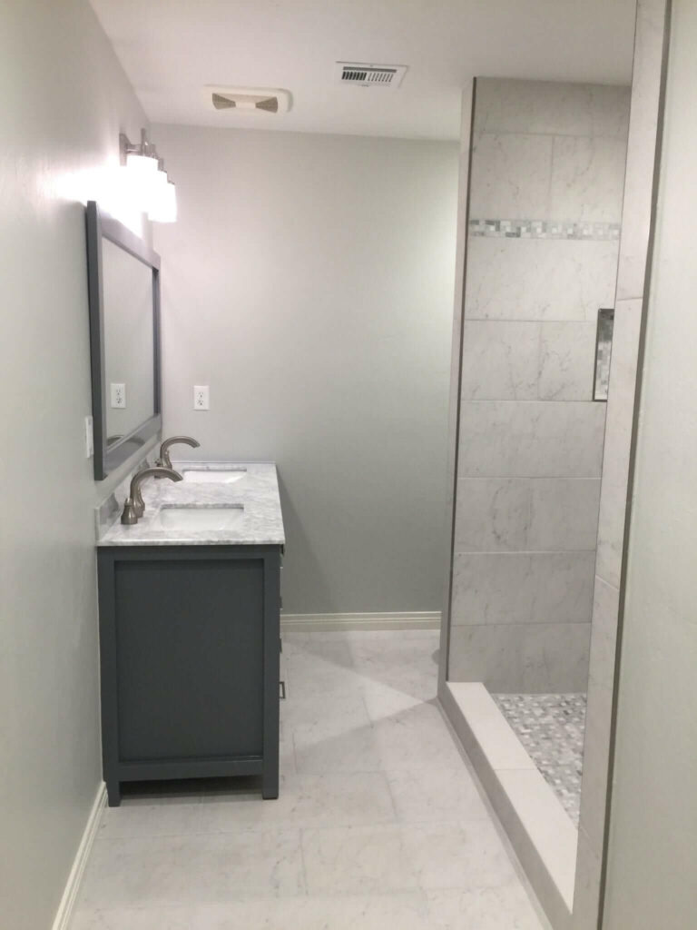 Bathroom remodeled with new tile floors, shower tile, glass shower door, counters, vanity, mirror, toilet, and lighting.