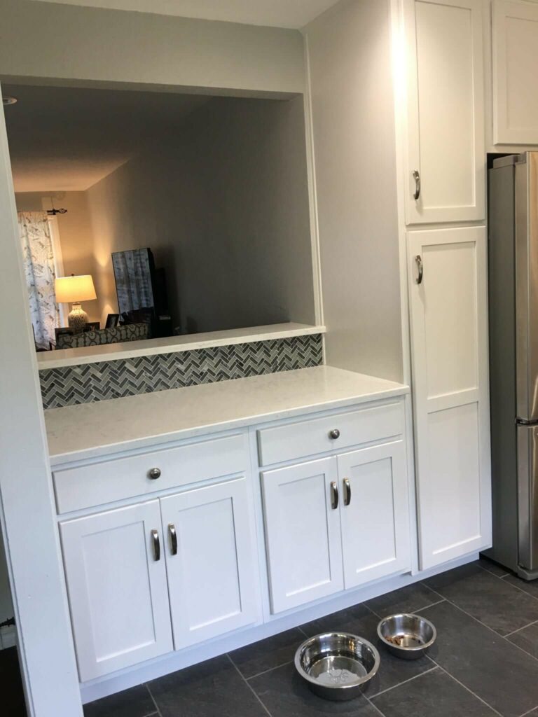 A kitchen remodeled including a new window from kitchen to living room, granite bar top, cabinets, vanity, backsplash tile, and floor tile.
