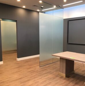 This commercial remodel includes a newly raised ceiling, lighting, flooring, and custom glass panels.