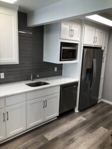 A commercial break room with a new backsplash, quartz counters, cabinets, engineered wood flooring, and appliances.