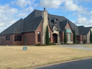 Large, elegant brick and stone home with a new Grand Manor Class IV impact-resistant shingle roof, located in Deer Creek. The home features high, steep rooflines and tall windows, showcasing quality construction and premium roofing material.