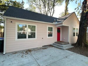 Remodeled 1927 Norman home with new pink siding, a red front door, new roof, windows, and concrete driveway.