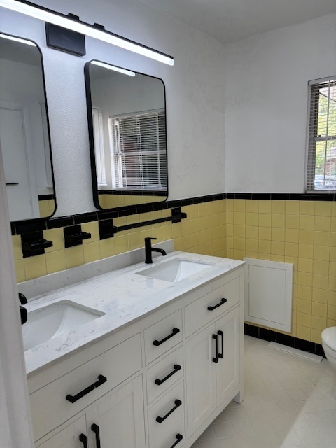 Updated bathroom with double-sink vanity, black hardware, framed mirrors, and yellow tile walls