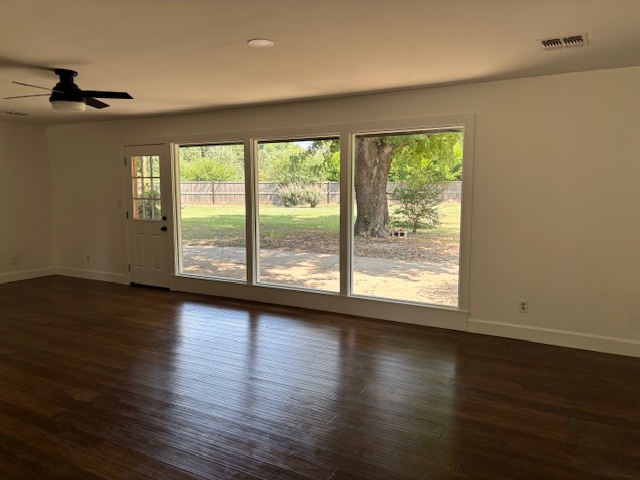 Remodeled living room with three new large windows, smaller exterior door, ceiling fan, and wood flooring