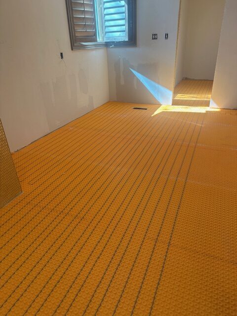 Bright orange Schluter-Ditra underlayment with embedded heating cables installed across a large master bathroom floor in Edmond, before tile placement.